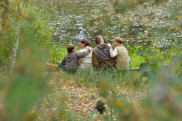 幸せな秋の森の湖のそばに座って家族の笑顔 — ストック写真