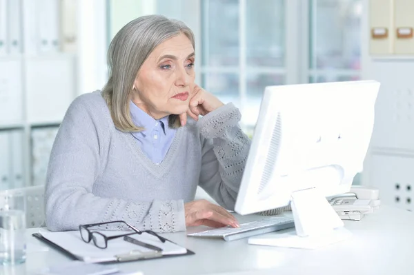 コンピューターを持つテーブルで働く年配の女性 — ストック写真