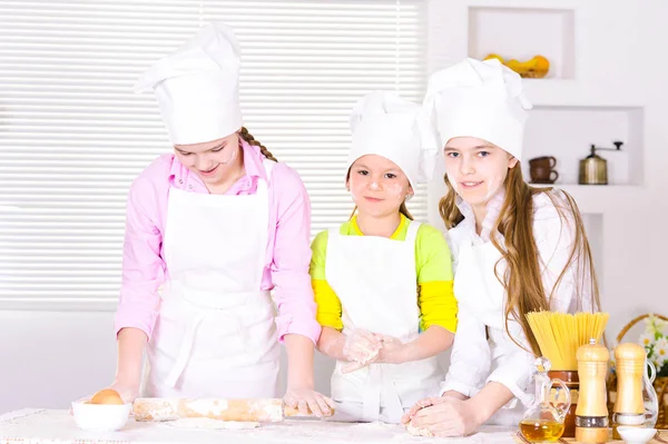 可爱的小女孩在厨师的帽子和围裙准备在家里的厨房面团 — 图库照片