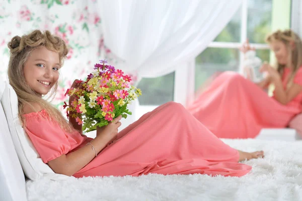 家でポーズの花の花束と美しいピンクのドレスの愛らしい少女 — ストック写真