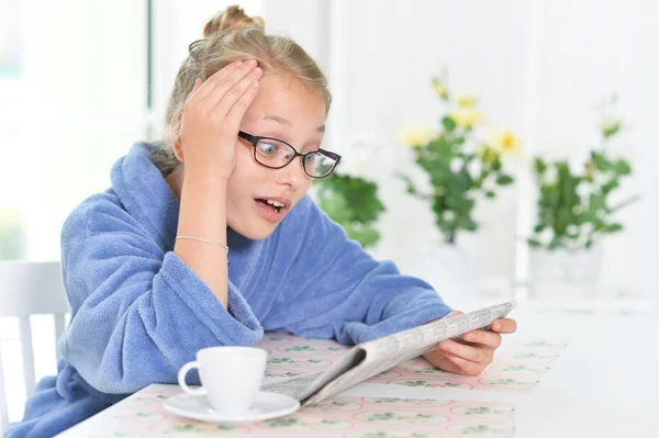 可爱的女孩在眼镜和蓝色浴袍读报纸 — 图库照片