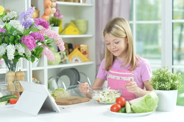 Симпатична Маленька Дівчинка Готує Свіжий Салат Кухонному Столі Планшетом Вдома — стокове фото