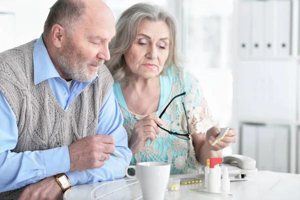 生病的老年妇女 丈夫坐在旁边 手里拿着药丸 — 图库照片
