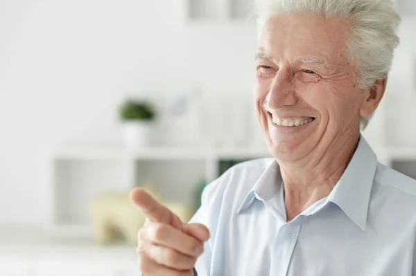 Portrét Usměvavého Staršího Muže Ukazujícího Prstem Doma — Stock fotografie