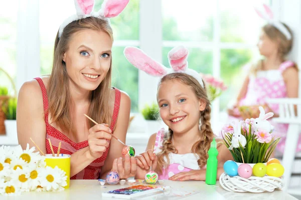 Mother with daughter wearing rabbit ears decorating  Easter eggs at home