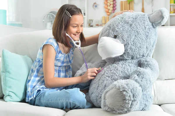 little girl  with stethoscope playing with  toy teddy  bear in facial mask