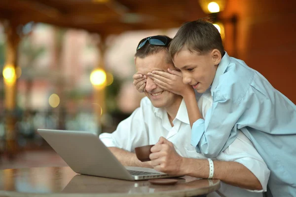 儿子和父亲在家里用笔记本电脑 男孩闭上了父亲的眼睛 — 图库照片