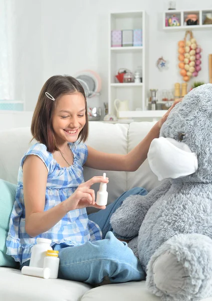 Petite fille jouant au docteur avec un ours jouet dans un masque facial — Photo