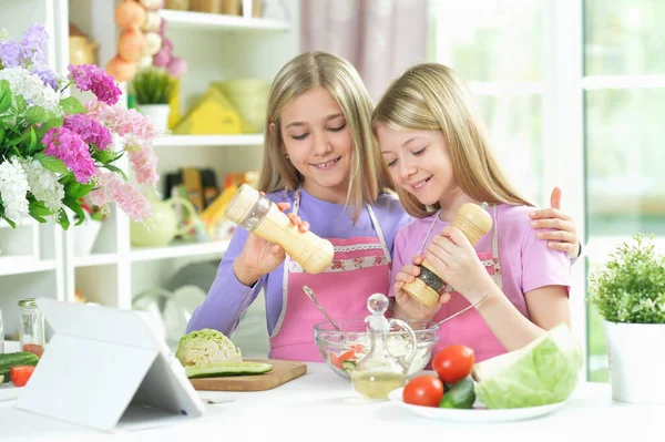 Dwie Dziewczyny Różowych Fartuchach Przygotowujące Sałatkę Stole Kuchennym Tabletką — Zdjęcie stockowe
