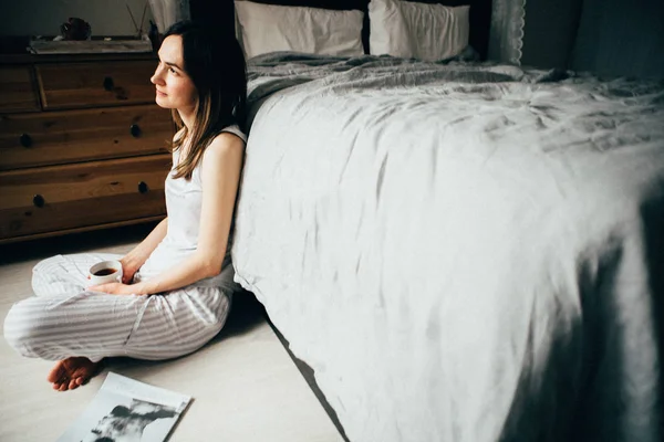 Mulher Sonolenta Com Xícara Café Inclinado Cama Enquanto Sentado Chão — Fotografia de Stock