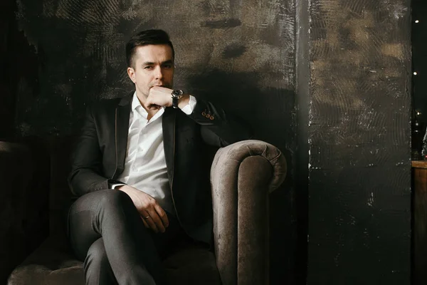 portrait of pensive businessman in suit sitting in velor armchair