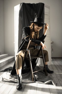 Moda tarzı giyinmiş çekici esmer kadın sandalyede oturuyor ve stüdyoda poz veriyor. 