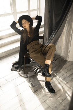 Moda tarzı giyinmiş çekici esmer kadın sandalyede oturuyor ve stüdyoda poz veriyor. 