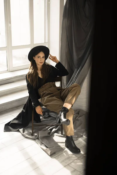 attractive brunette woman in fashion style clothes sitting on chair and posing in studio