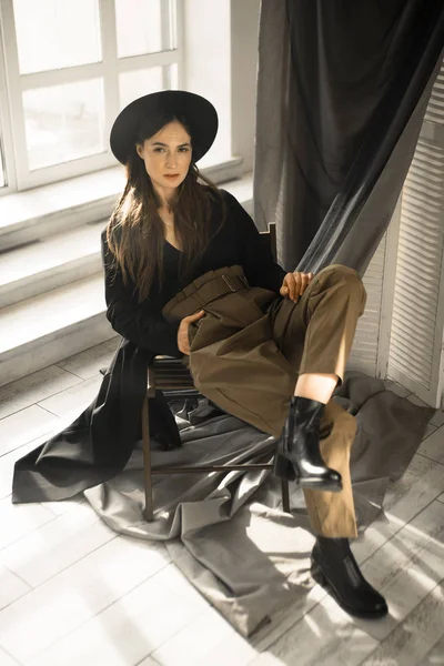 attractive brunette woman in fashion style clothes sitting on chair and posing in studio