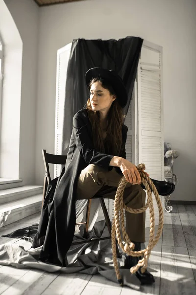 attractive brunette woman in fashion style clothes sitting on chair and posing in studio