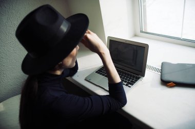Şapkalı moda kadını stüdyoda dizüstü bilgisayarda çalışıyor. 