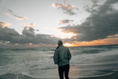 Güzel gün batımında kumlu sahilde yürüyen bir kadın.