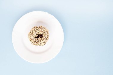 Çörek çikolata sır ile kaplı ve mavi bir masada beyaz tabaklar fındık serpilir