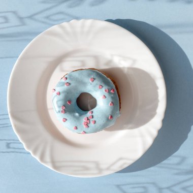 Çörek mavi sır ile kaplı ve gölgeler in numune yüzeyi ile doğal ışık altında mavi zemin üzerine beyaz bir plaka üzerinde küçük pembe kalpler serpilir