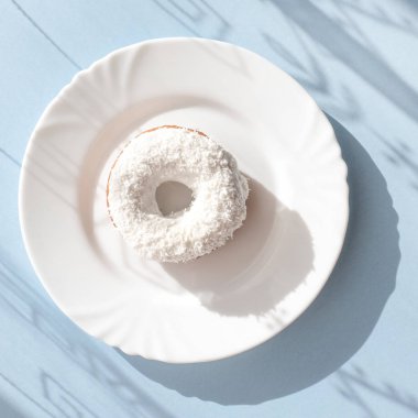 Çörek beyaz sır ile kaplı ve Hindistan cevizi pul gölgeler in numune yüzeyi ile doğal ışık altında mavi zemin üzerine beyaz bir tabakta serpilir