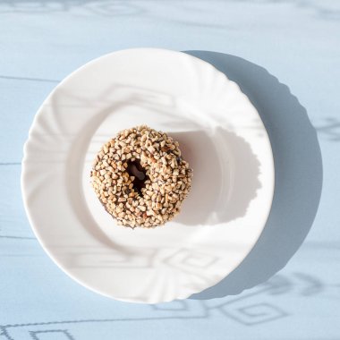 Çörek çikolata sır ile kaplı ve gölgeler in numune yüzeyi ile doğal ışık altında mavi zemin üzerine beyaz plaka üzerinde fındık serpilir