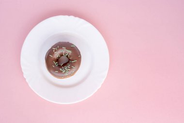 Çörek çikolata sır ile kaplı ve pembe bir arka plan üzerinde beyaz plaka üzerinde yeşil tüp ile serpilir