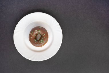 Çörek çikolata sır ile kaplı ve siyah arka plan üzerine beyaz plaka üzerinde yeşil tüp ile serpilir