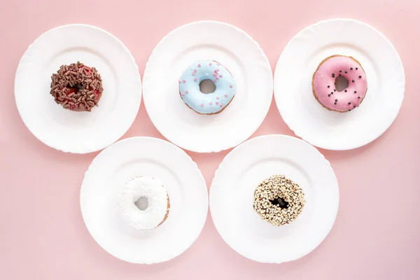 Cinco platos blancos con diferentes rosquillas cubiertas con esmalte sobre fondo rosa — Foto de Stock