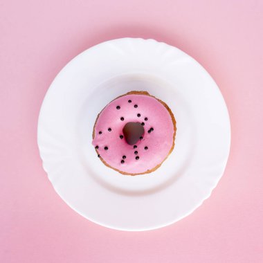 Çörek pembe buzlanma ile kaplı ve pembe bir arka plan üzerinde beyaz plaka üzerinde siyah madalyonun serpilir