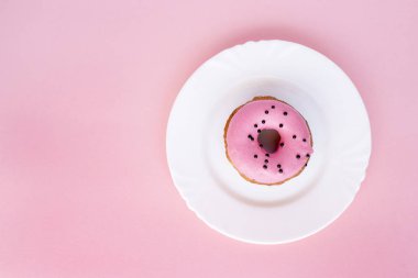 Çörek pembe buzlanma ile kaplı ve pembe bir arka plan üzerinde beyaz plaka üzerinde siyah madalyonun serpilir