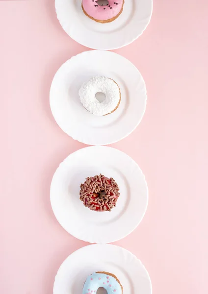 एक गुलाबी टेबल पर सफेद प्लेटों पर ग्लास से ढके हुए डोनट — स्टॉक फ़ोटो, इमेज