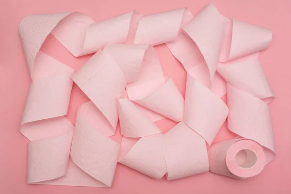 A rolled-out roll of pink toilet paper on a pink background. Hygiene products.