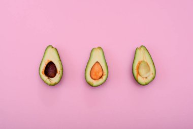 Avokado doğal rengi ve durumu pembe arka planda ikiye bölünmüş. Kemiklerle ya da kemiksiz. Üç..