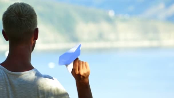 Movimento lento. Jovem lança avião de papel contra lago, como na infância — Vídeo de Stock