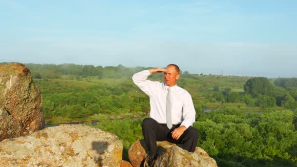 Business man sits at mountain top and see afar. 4K 3840x2160 — стоковое видео