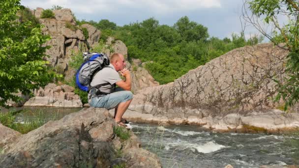Nadenkende man toeristische met rugzak zitten op steen in de buurt van river.4k 3840 x 2160 — Stockvideo