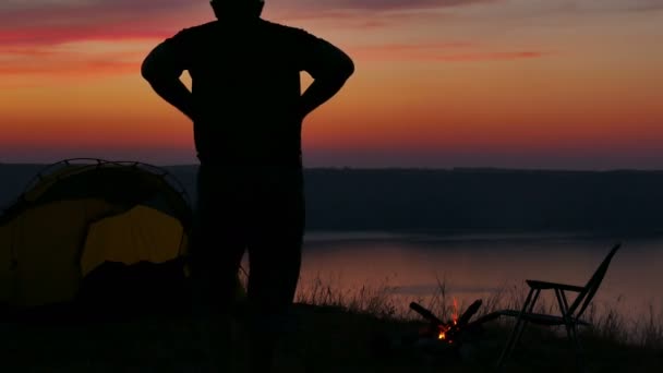 4K Tenda, fogueira, nascer do sol e siluuette homem perto do lago . — Vídeo de Stock