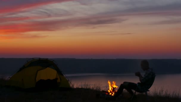 4k. Mann wartet Sonnenaufgang mit Kaffee oder Tee in der Nähe des Sees. — Stockvideo