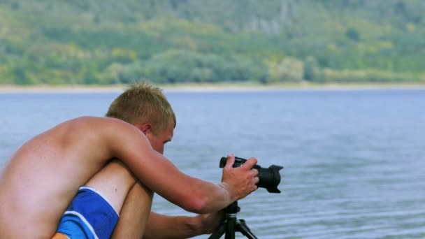 4 k. kille fotograf justerar kameran på stranden av sjön — Stockvideo