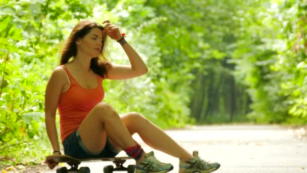 4K. Young beautiful girl sits on  skateboard in park — Stock Video