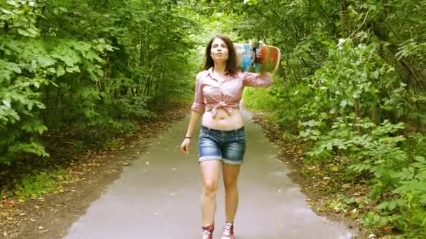 4K. Joven hermosa chica va con monopatín en el parque de verano — Vídeo de stock