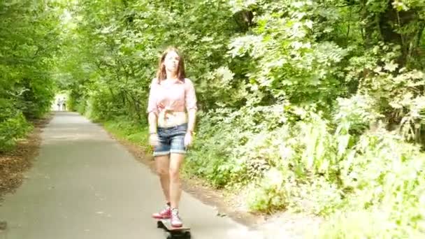 4К. Молодая красивая девочка-подросток ходит на скейтборд в летний парк — стоковое видео