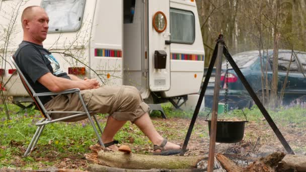 Disparo de 4K. Hombre feliz en la vida al aire libre en caravana, remolque. Pilaf en madera — Vídeos de Stock