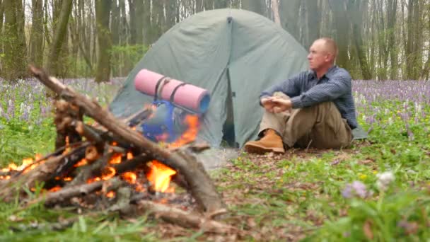 4K. Homme adulte assis dans le bois près du feu de camp et tente . — Video