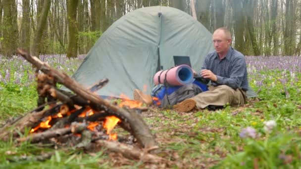4K.Man tourist  near campfire work portable computer in wood. — Stock Video