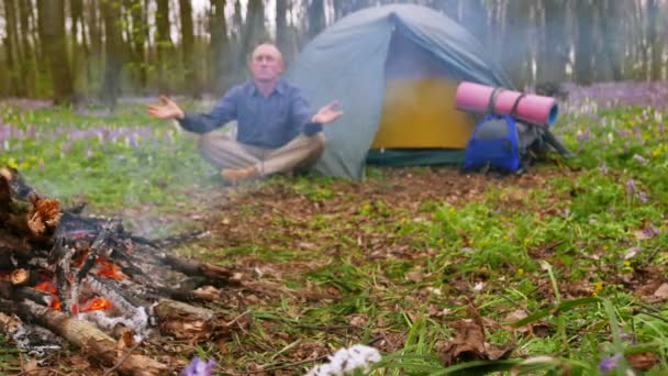 4K. Homme adulte médite dans le bois près du feu de camp et tente.Dolly shot — Video