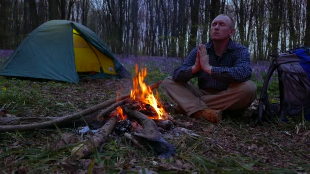 4K. Adult man meditates in wood  near campfire and tent. — Stock Video