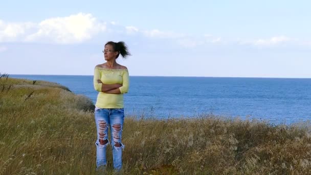 4k. erwachsene Frau in gelber Bluse steht an windigem Tag gegen die Meeresoberfläche — Stockvideo