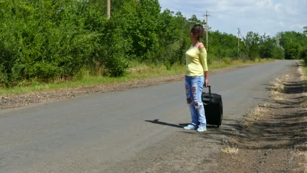 4К. Зрелая взрослая женщина с чемоданом, останавливающимся на дороге. Автостопом . — стоковое видео